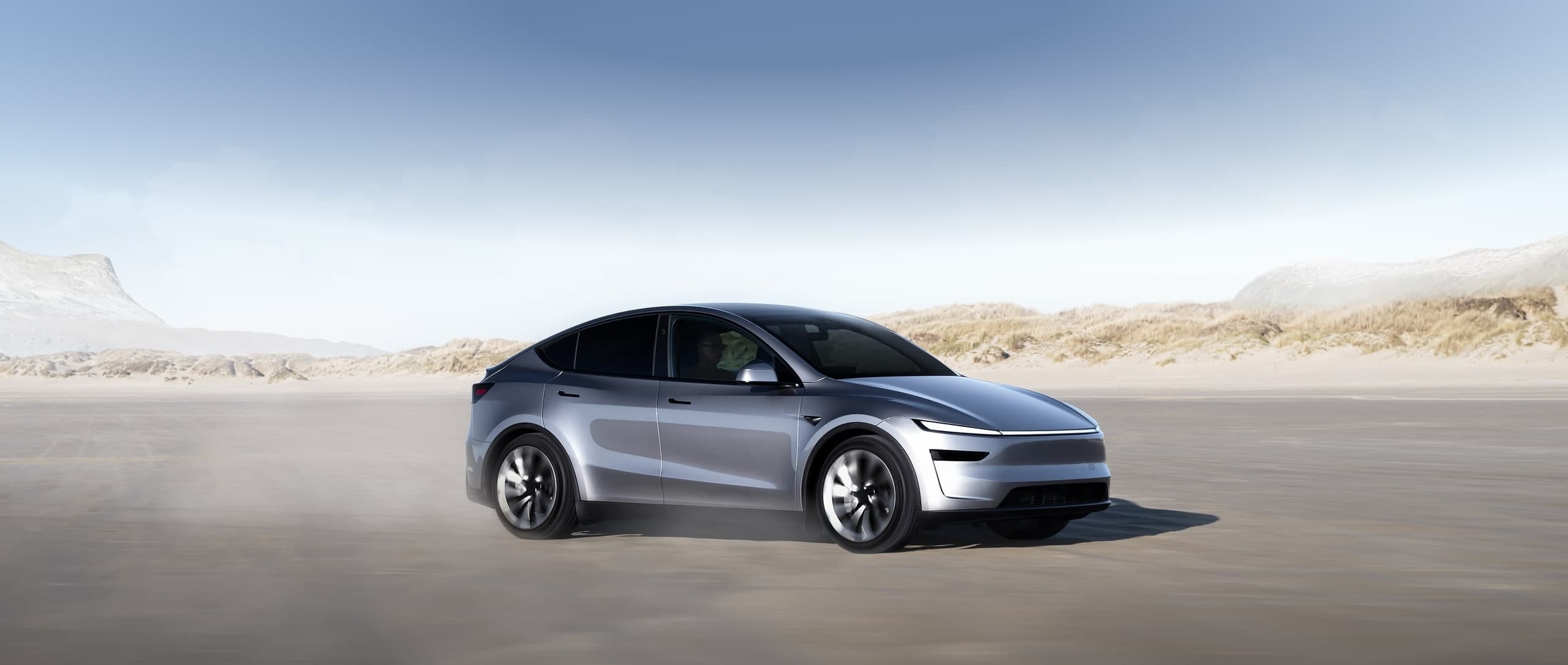 Tesla Model Y warna perak, memandu di jalan pantai