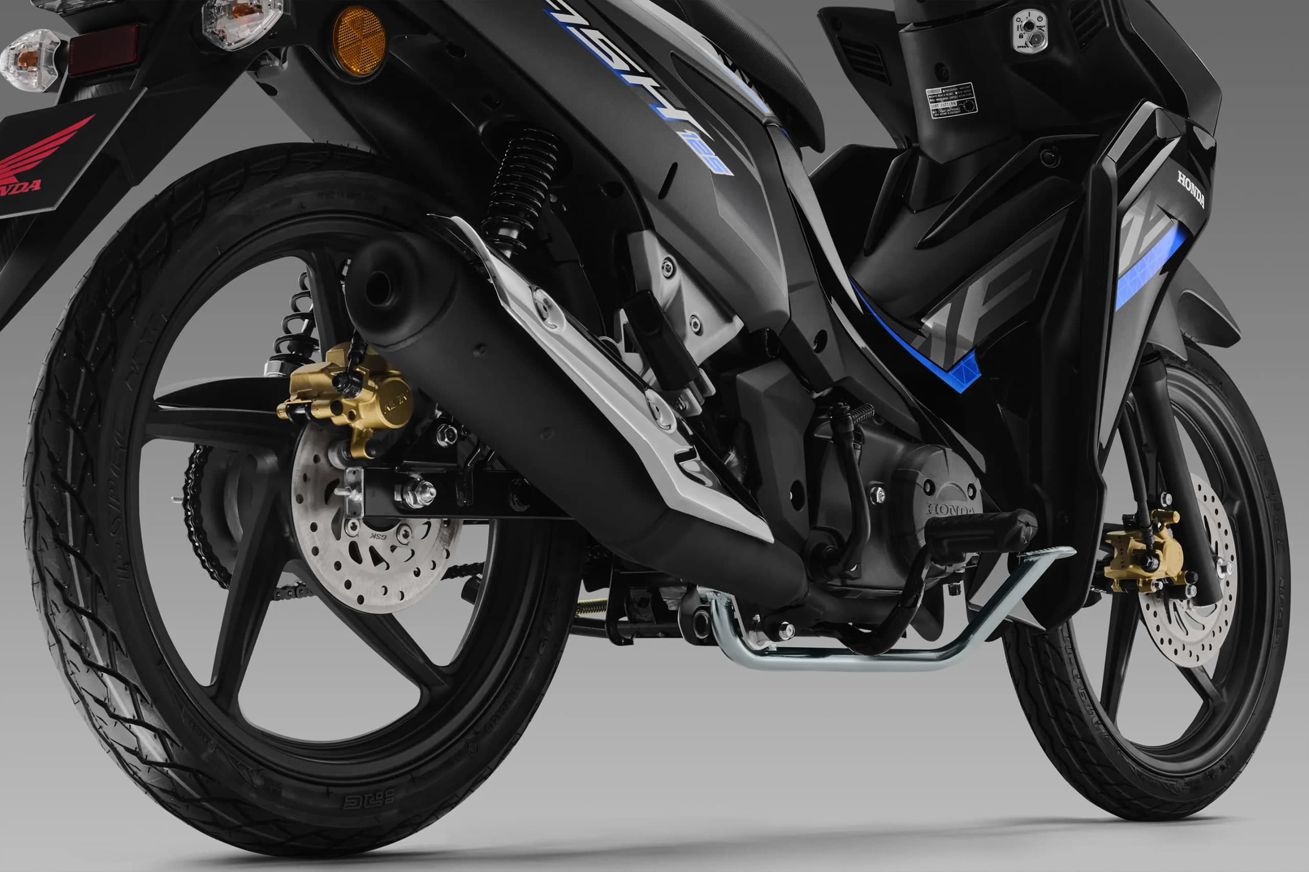 Roda belakang Honda Dash 125 dengan kaliper brek emas, ekzos hitam serta rantai dan sproket kelihatan