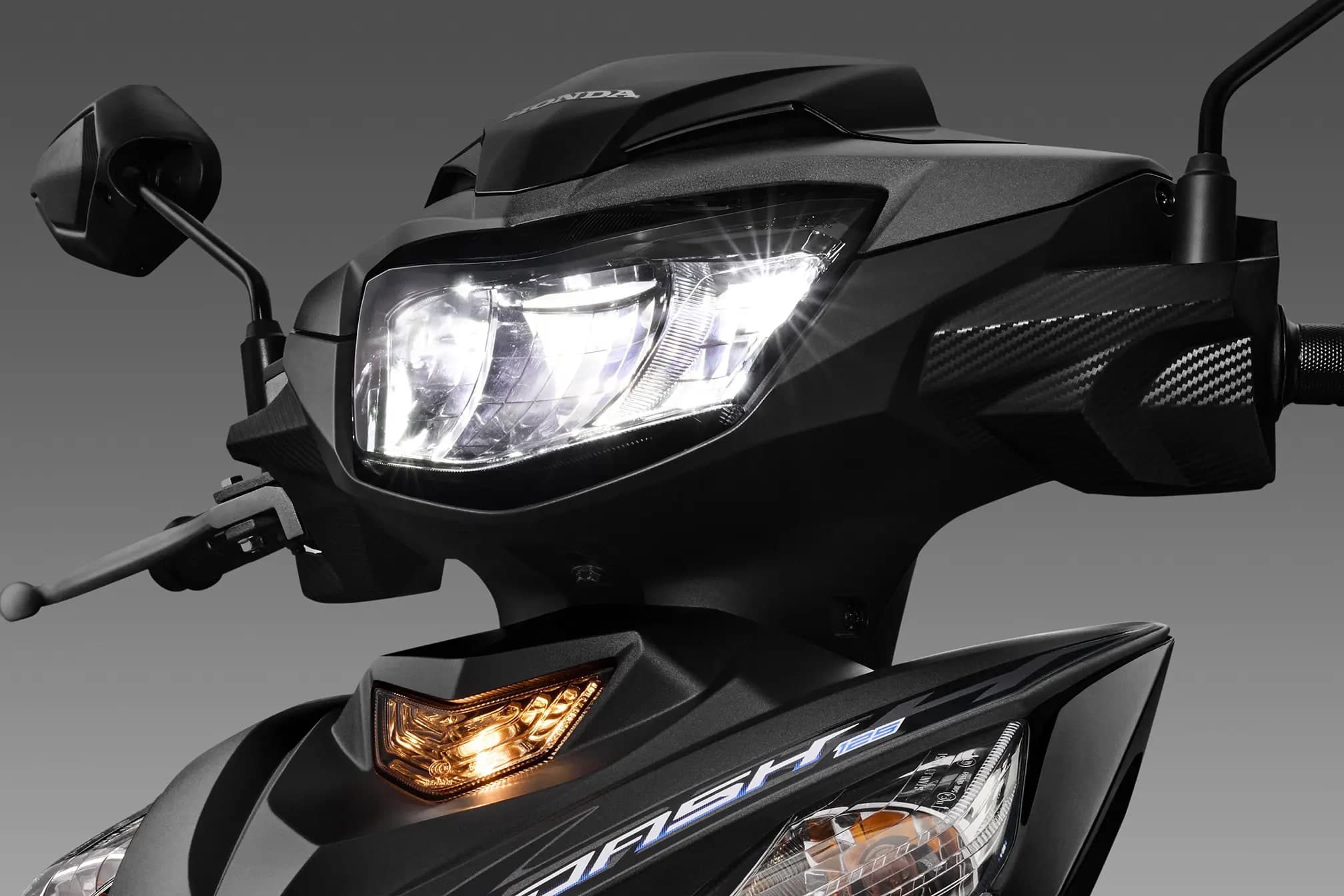 Lampu utama LED Honda Dash 125 menyala pada kaus hadapan hitam matte, lencana HONDA dan decal DASH 125 kelihatan