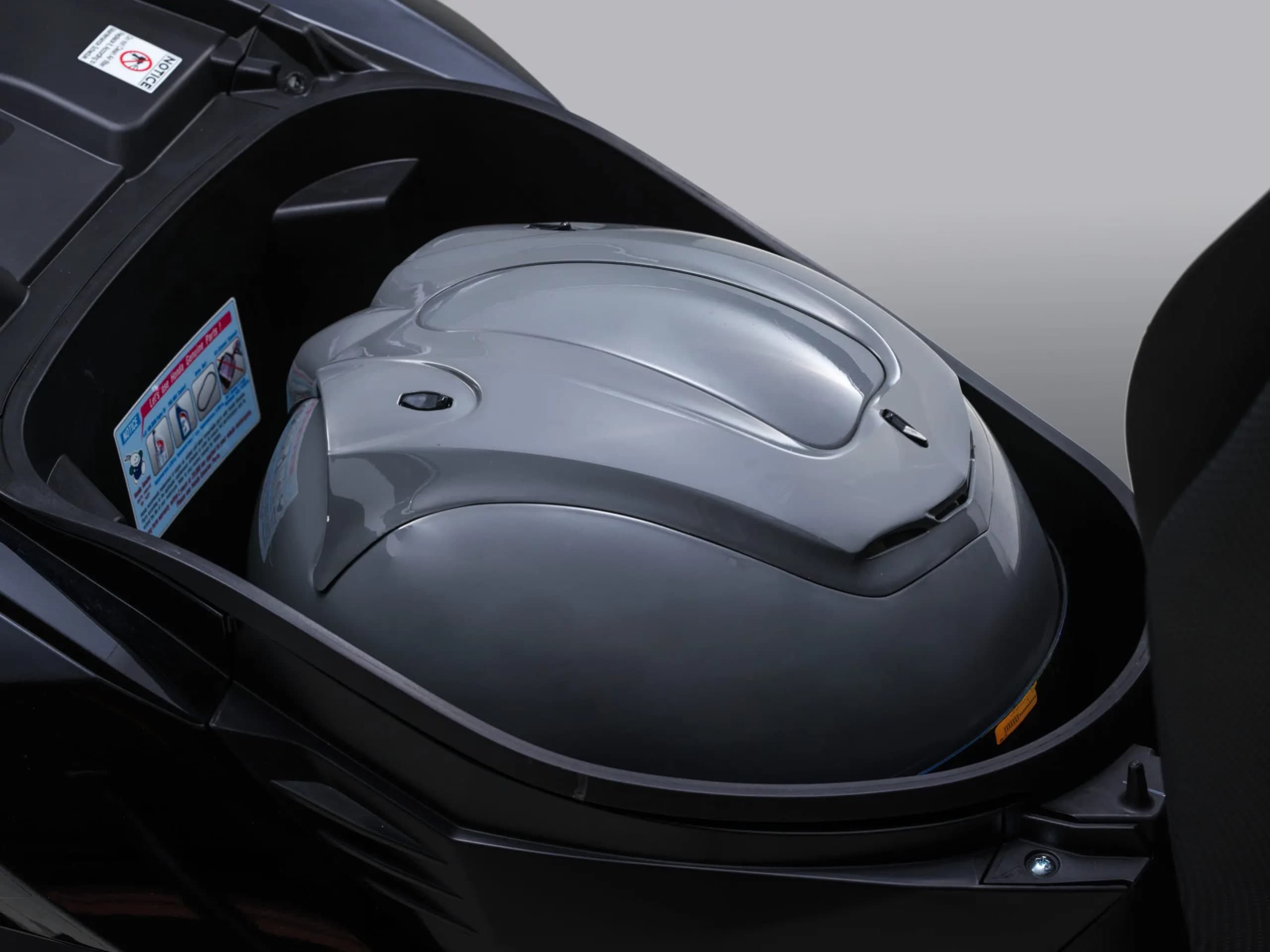 Ruang simpanan bawah tempat duduk Honda Vario 125 terbuka dengan sebuah topi keledar muka penuh di dalamnya