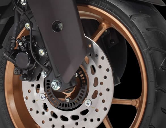 Roda hadapan Yamaha NMAX dengan kaliper brek cakera dan rim aloi gangsa, menunjukkan sistem ABS dua saluran