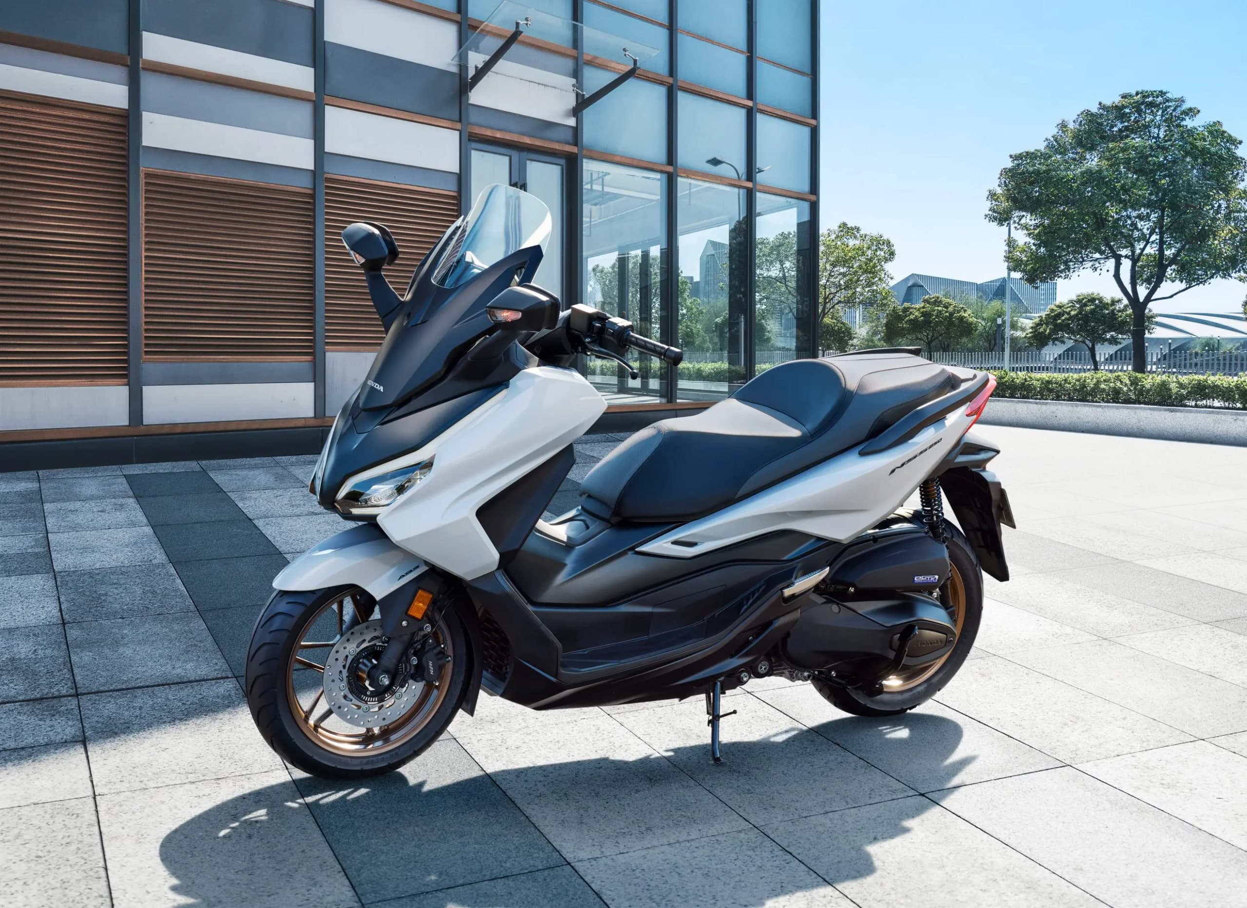 Honda NSS250 warna putih pearl diparkir di plaza berturap batu di hadapan bangunan pejabat berkaca, pandangan sisi kanan