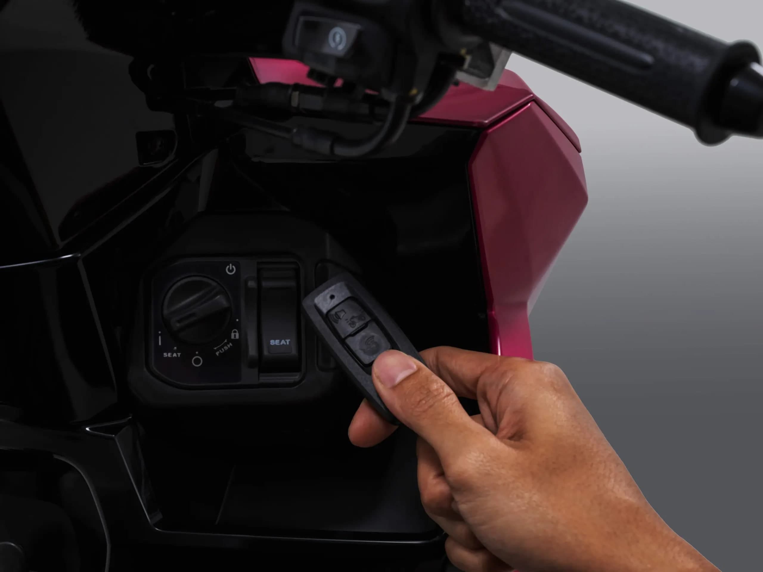 Suis ignisi keyless Honda Vario 125 pada badan merah jambu, tangan memegang kunci pintar hitam