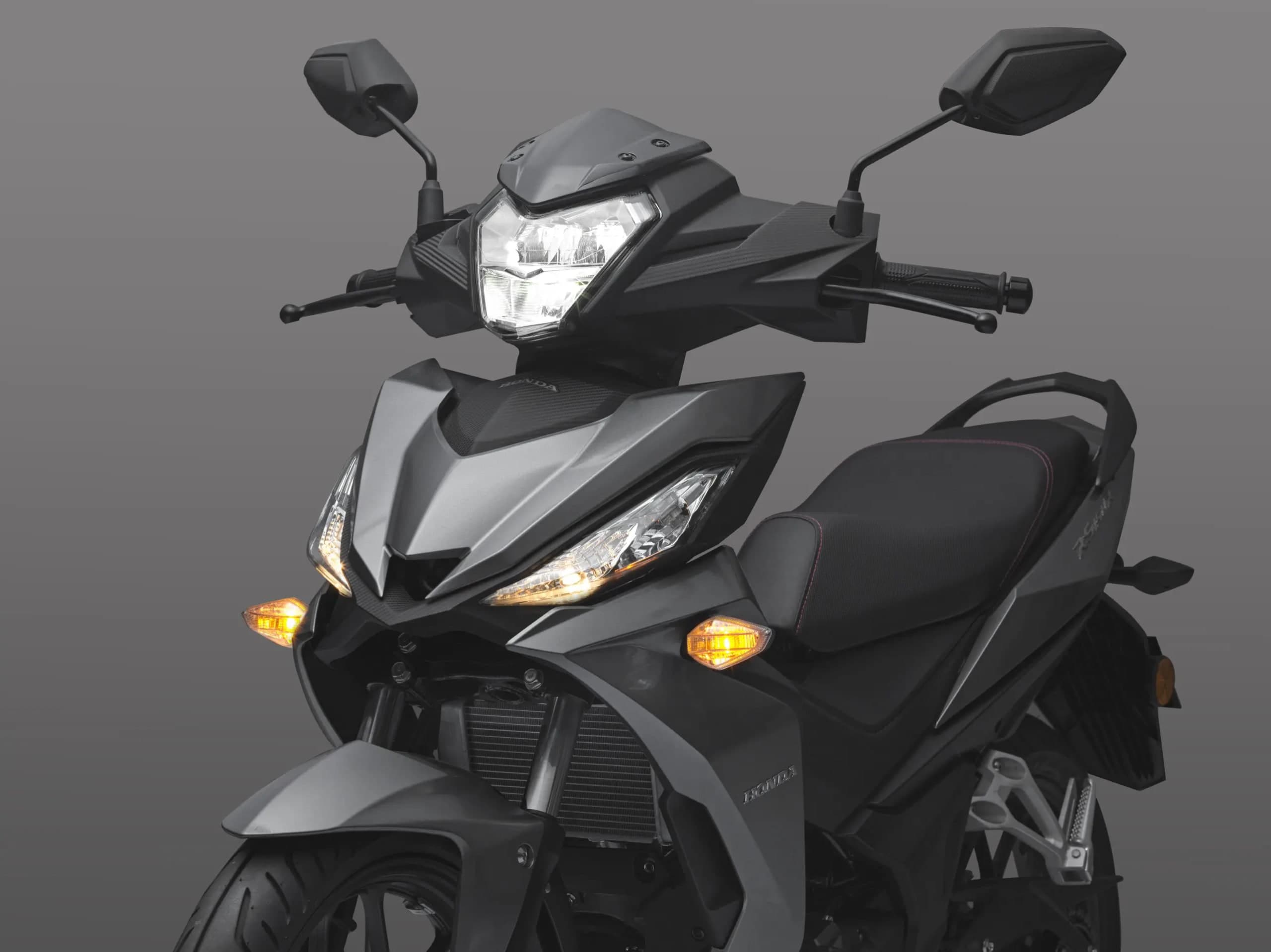 Lampu utama LED Honda RS150R menyala pada fairing hitam matte, cermin sisi dan lampu isyarat kelihatan